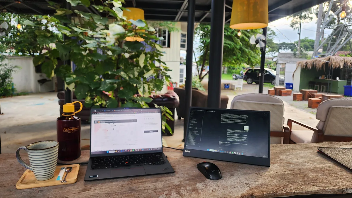 Laptop and portable monitor set up on a timber table in the outdoor seating area at Ciao 24 Hour Cafe in Chiang Mai
